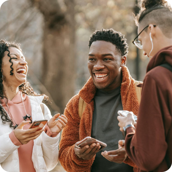 Three people outside, each holding a phone, all are laughing. 